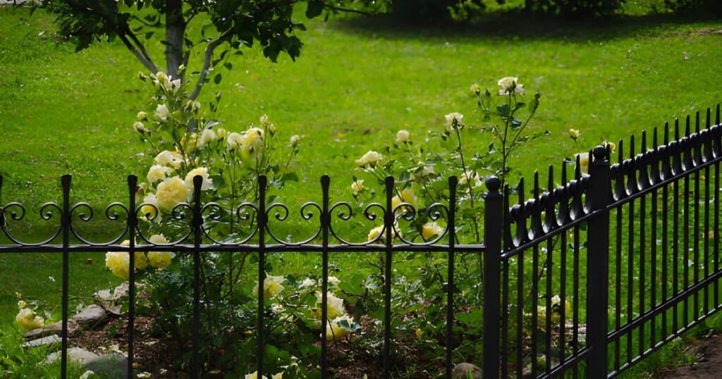reja de herreria frente a flores y arboles en jardin Reja de herrería frente a flores y árboles en un jardín
