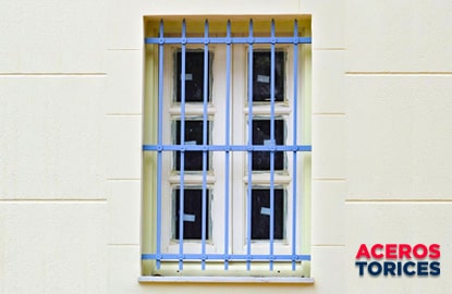 Una ventana de herrería con barrotes azules en forma de punta como protección