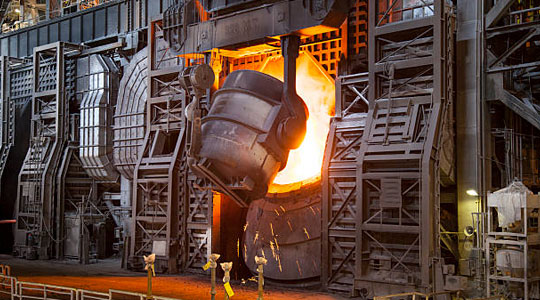 Recipiente metálico vertiendo hierro fundido dentro de un horno para la fabricación del acero - precios del acero